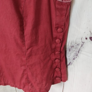 May include: A red sleeveless vest with a velvet trim and button fastenings on the side.