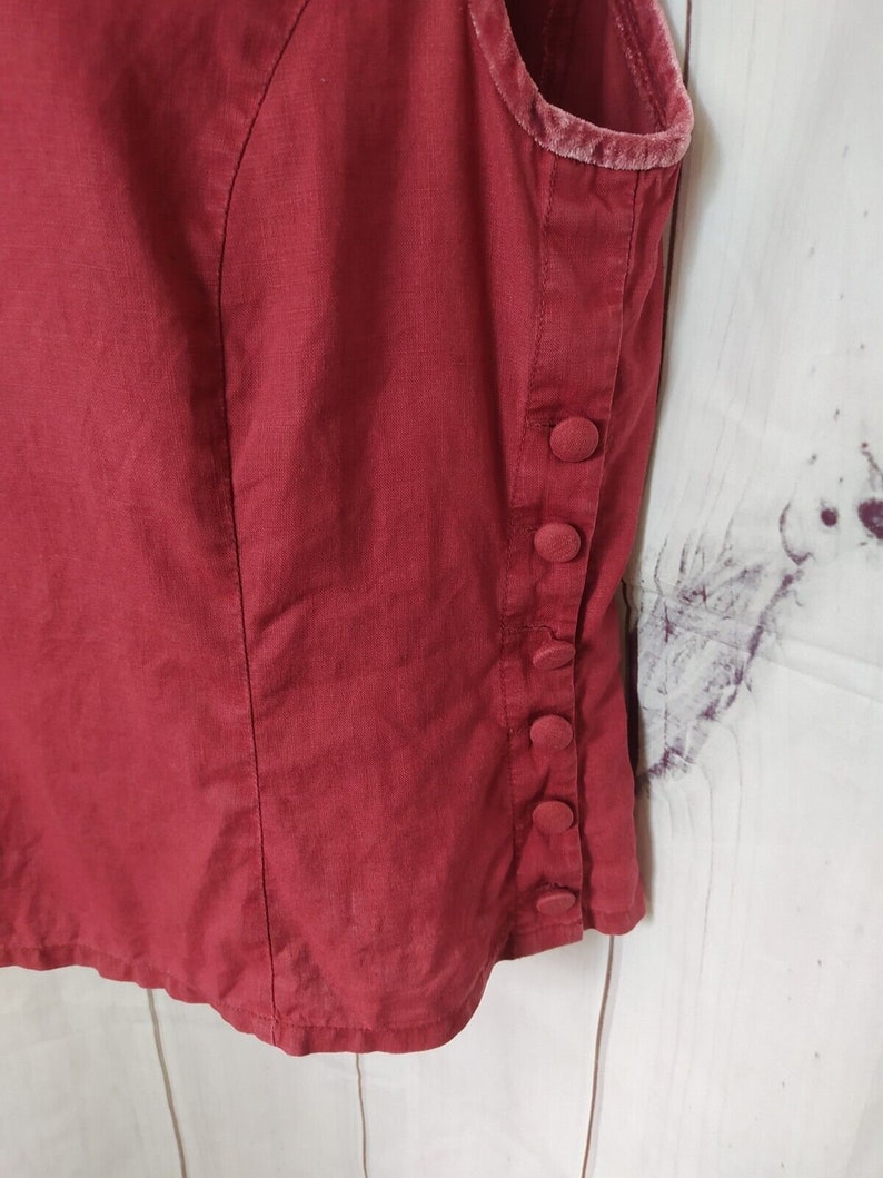 May include: A red sleeveless vest with a velvet trim and button fastenings on the side.