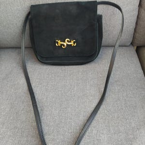 May include: A black suede crossbody bag with a gold metal clasp. The bag has a long adjustable strap.