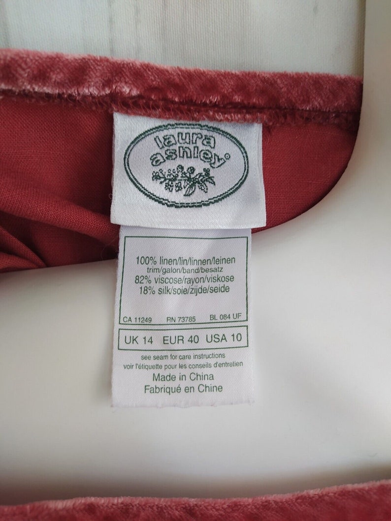May include: A white tag with the Laura Ashley logo and size information. The tag reads "100% linen/lin/linnen/leinen trim/galon/band/besatz 82% viscose/rayon/viskose 18% silk/soie/zijde/seide CA 11249 RN 73785 BL 084 UF UK 14 EUR 40 USA 10 see seam for care instructions voir l'&eacute;tiquette pour les conseils d'entretien Made in China Fabriqu&eacute; en Chine"