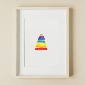 May include: A framed watercolor print featuring a stack of colorful rings, resembling a classic toy. The rings are arranged in a pyramid shape, with a small golden circle at the top. The colors include red, orange, yellow, green, blue, and purple.