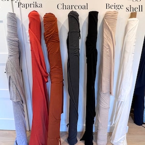 Puede incluir: Ocho rollos de tela en varios colores, incluyendo gris, paprika, &oacute;xido, carb&oacute;n, negro, beige arena y c&aacute;scara de huevo. La tela est&aacute; enrollada y colgando de una pared blanca.