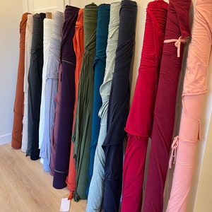 Puede incluir: Una colecci&oacute;n de rollos de tela en varios colores, incluyendo rojo, rosa, azul, verde y marr&oacute;n. Los rollos est&aacute;n dispuestos verticalmente y est&aacute;n atados con cuerda.