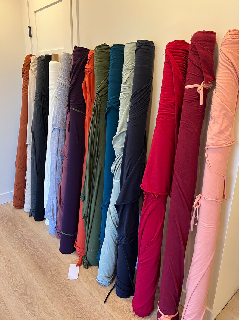 Puede incluir: Una colecci&oacute;n de rollos de tela en varios colores, incluyendo rojo, rosa, azul, verde y marr&oacute;n. Los rollos est&aacute;n dispuestos verticalmente y est&aacute;n atados con cuerda.