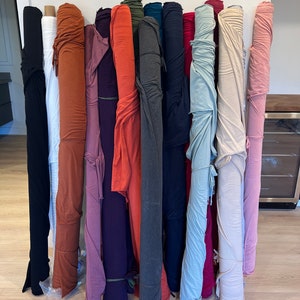 Puede incluir: Una colecci&oacute;n de rollos de tela en varios colores, incluyendo blanco, naranja, morado, rojo, gris, azul y rosa. Los rollos est&aacute;n apilados contra una pared blanca.