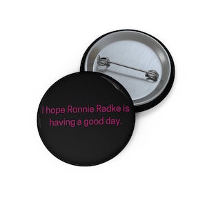 May include: Black button with a pink message that reads "I hope Ronnie Radke is having a good day."