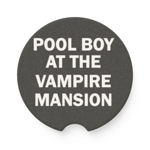 Puede incluir: Un posavasos redondo negro con el texto "POOL BOY AT THE VAMPIRE MANSION" en blanco.