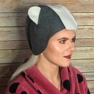 May include: A gray and white felt hat with ear flaps. The hat has a unique design with a pointed top and a curved brim.
