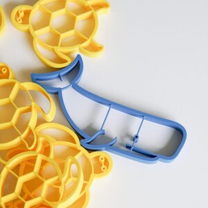 Puede incluir: Un juego de cortadores de galletas de plástico amarillo en forma de tortuga y un cortador de galletas de plástico azul en forma de ballena.