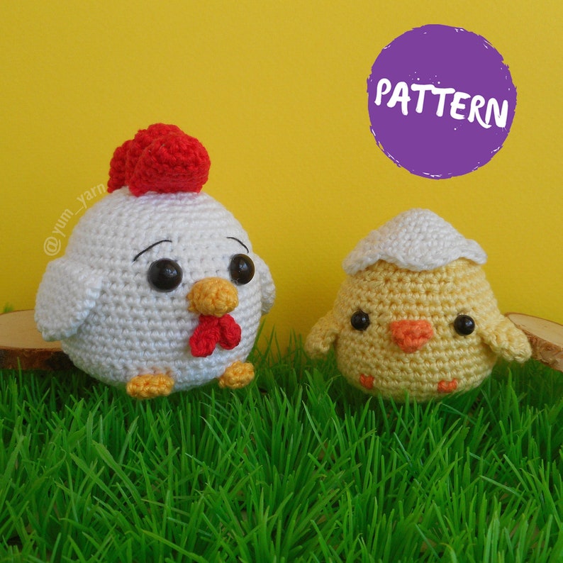 May include: A white crocheted chicken with a red comb and a yellow beak sits next to a yellow crocheted chick with a white eggshell. The toys are sitting on green grass.