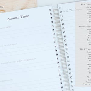 May include: A spiral-bound pregnancy journal with white pages featuring black text. The left page shows the heading Almost Time with prompts for excitement, nerves, and pregnancy memories. The right page lists contents for the first, second, and third trimesters.