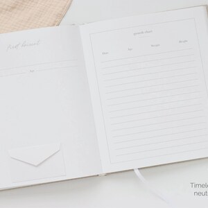 May include: An open memory book with light beige covers featuring two pages. The left page is titled First Discoveries with fields for date and age. The right page is titled Growth Chart with columns for date, age, weight, and height. A small white envelope is attached to the left page.