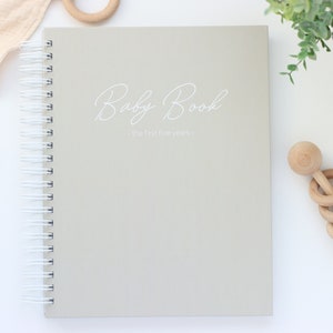 May include: A gray spiral bound baby book with the text "Baby Book - The first five years -" printed in white on the cover.