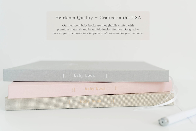 May include: Three rectangular baby books stacked horizontally, featuring gray, light pink, and beige covers. Each spine displays the text "baby book" with vertical lines. Above the stack, text reads "Heirloom Quality + Crafted in the USA."