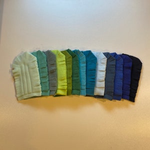 May include: A set of 12 felt fabric strips in a gradient of green, blue, and purple shades. The strips are fringed on one side and have a smooth, velvety texture.