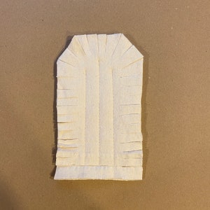 Op de afbeelding: Een witte stoffen deurstopper met een franje rand. De deurstopper is boogvormig.