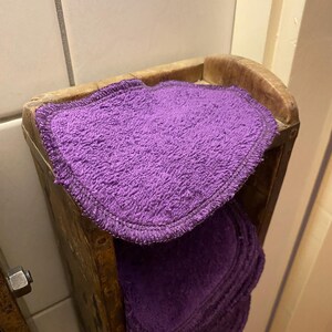 Op de afbeelding: Een stapel herbruikbare make-up remover pads in paars in een houten houder.