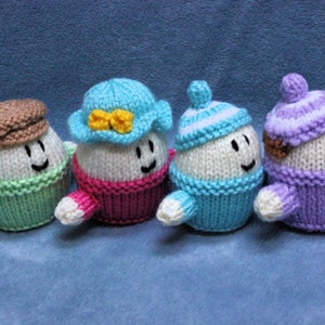 May include: Four knitted egg-shaped toys with different colored hats and sweaters. The toys have smiling faces and are arranged in a row.