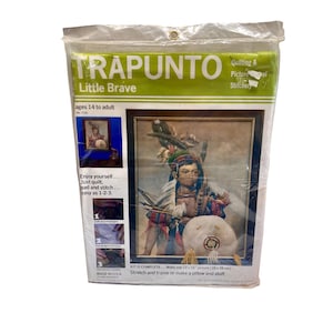 Pode incluir: Uma embalagem selada para um kit de acolchoado e bordado Trapunto Little Brave. O kit inclui uma imagem emoldurada de uma pessoa nativa americana. O texto da embalagem inclui "idades 14 a adulto" e "Made in USA". A imagem tem 28 x 38 cm.