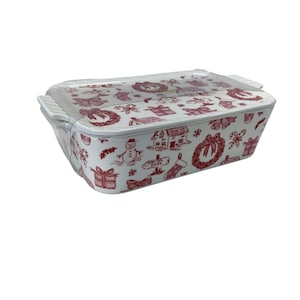 May include: A rectangular white ceramic baking dish with a clear lid. The dish is decorated with a repeating pattern of red Christmas-themed illustrations, including wreaths, gifts, and snowmen. The dish has handles on each side.
