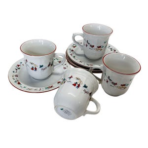 May include: A set of white ceramic teacups and saucers. The cups and saucers have a red trim and are decorated with a colorful pattern of figures and trees. The set includes four cups and saucers.