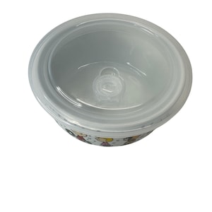 Puede incluir: Un cuenco de cer&aacute;mica blanca con una tapa de pl&aacute;stico transparente. El cuenco tiene un dise&ntilde;o de dibujos animados alrededor del borde. La tapa tiene un peque&ntilde;o asa de pl&aacute;stico transparente en el centro. El cuenco es redondo y tiene una superficie lisa.
