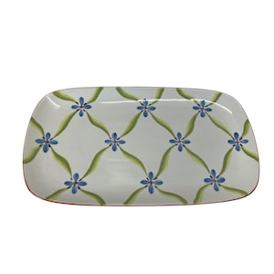 May include: Rectangular serving platter with a white background, featuring a repeating pattern of blue flowers and green vines. The edges are trimmed with a red border. A decorative piece for serving food.