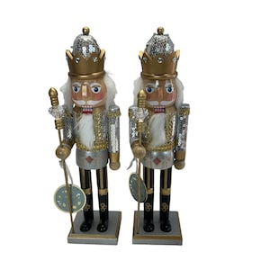 Könnte beinhalten: Zwei silberne und goldene Nussknackerfiguren mit Paillettenakzenten und weißen Bärten. Jeder Nussknacker hält einen goldenen Stab mit einer Kristallspitze.