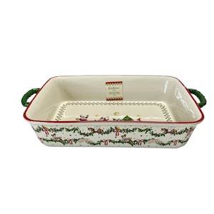 Puede incluir: Fuente rectangular de cerámica con interior blanco y borde rojo. La fuente presenta asas verdes y un diseño navideño festivo con Papá Noel, renos y árboles. La fuente mide aproximadamente 30 cm de largo.