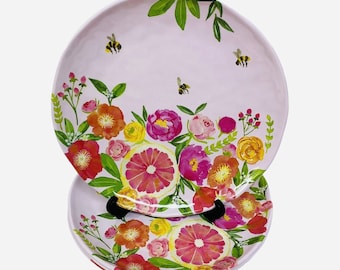 May include: Set of three pink floral dinner plates with a grapefruit design. The plates feature a pink, yellow, and green floral pattern with bees and leaves.