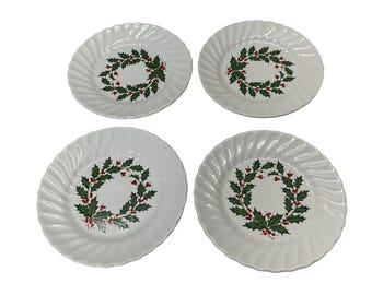 May include: Four white ceramic plates with a spiral edge design. Each plate features a central wreath design of green leaves and red berries, perfect for holiday dining. The plates are arranged on a white background.