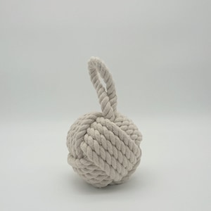 Pode incluir: Um pára-porta de corda branca com um design de nó e uma alça de laço.