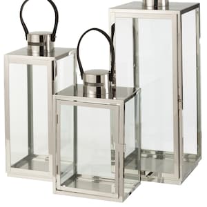 Könnte beinhalten: Drei silberne Metall-Kerzenlaternen mit schwarzen Griffen. Die Laternen sind in verschiedenen Größen und in einer Reihe vom größten zum kleinsten angeordnet.