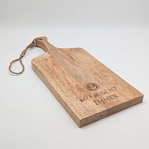 May include: A wooden cutting board with a rope handle. The board has a nautical theme with an anchor and the text "Meer Geht Immer".