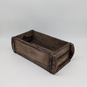 Può includere: Una scatola di legno rustica con accenti in metallo. La scatola è rettangolare con bordi arrotondati e ha una finitura in legno naturale.