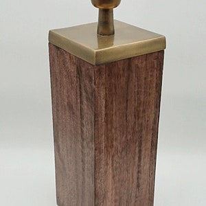 May include: A wooden table lamp with a brass base and a black lampshade. The lamp has a square base and a round top.