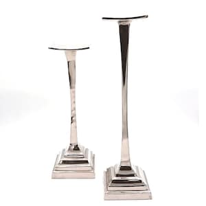 May include: Two silver metal candle holders with square bases and a tall, slender design. The taller candle holder is on the right and the shorter candle holder is on the left.