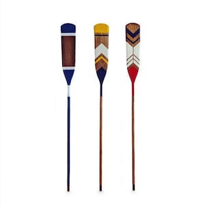 Peut inclure: Trois rames décoratives en bois avec des motifs peints. L'une présente un design bleu et blanc, une autre un motif chevron jaune et blanc, et la troisième un motif chevron rouge et blanc. Les rames ont de longs manches en bois fins.