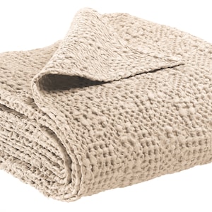 Könnte beinhalten: Eine beige gestrickte Wolldecke mit einem strukturierten Waffelmuster. Die Decke ist gefaltet und auf einem weißen Hintergrund abgebildet.