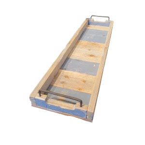 May include: A long, rectangular wooden serving tray with a distressed finish. The tray features natural wood tones, accented by sections of blue-gray paint. It has metal handles on each end, perfect for carrying food or decor.