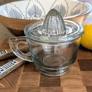 Op de afbeelding: Een witte keramische mok met een zwart handvat en de tekst "But First, Coffee" in een handschriftstijl. De mok staat op een wit oppervlak. De mok is 10 cm hoog.