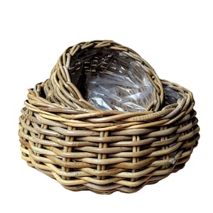 Puede incluir: Dos cestas de mimbre tejidas, una anidada dentro de la otra. Las cestas están hechas de mimbre de color marrón claro, de aspecto natural y tienen forma redonda. La cesta interior contiene un forro de plástico transparente. Las cestas son adecuadas para almacenamiento o decoración.