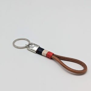 May include: A brown leather keychain with a silver key ring and a braided strap with red, white, and blue accents.