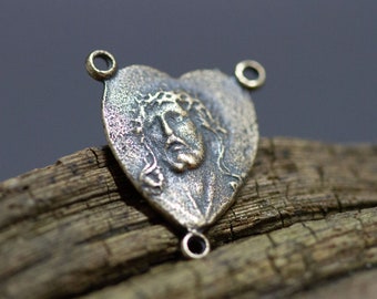 May include: A heart-shaped metal charm featuring a detailed image of Jesus Christ wearing a crown of thorns. The charm has two rings at the top and one at the bottom.