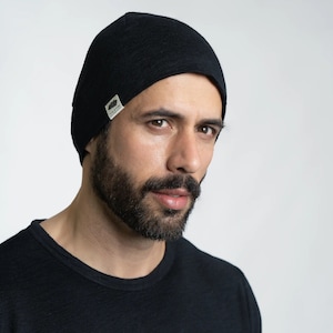 Könnte beinhalten: Eine schwarze Mütze mit einem kleinen, rechteckigen Etikett an der Seite. Die Mütze ist aus weichem, gestricktem Stoff und hat ein schlichtes, klassisches Design.