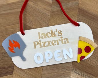May include: Wooden sign for Jack's Pizzeria with the text "Jack's Pizzeria OPEN". The sign has a red cord for hanging, a pizza slice, and a pizza peel with flames.