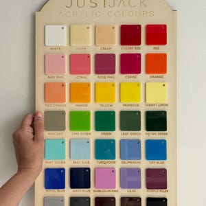 May include: A wooden display board featuring a variety of acrylic color swatches. The board is labeled "JUSTJACK ACRYLIC COLOURS" and includes a range of colors from white and ivory to black and maroon. A hand is holding the board.