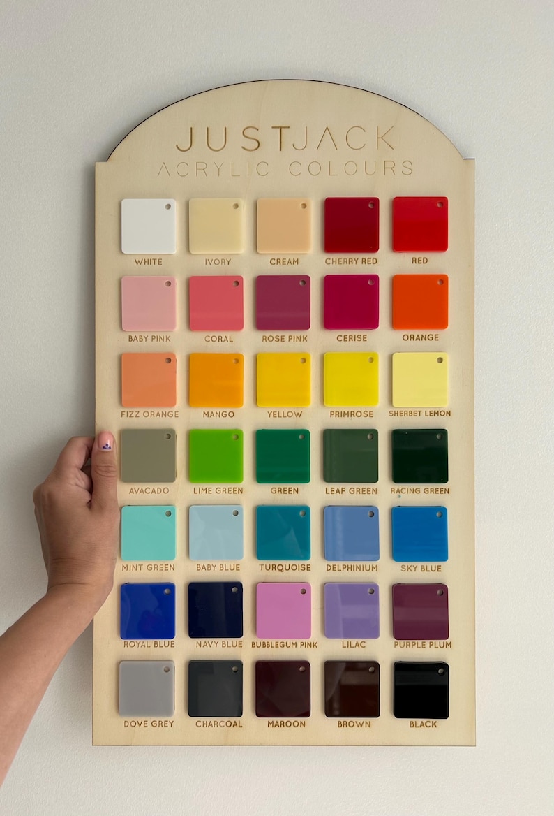 May include: A wooden display board featuring a variety of acrylic color swatches. The board is labeled "JUSTJACK ACRYLIC COLOURS" and includes a range of colors from white and ivory to black and maroon. A hand is holding the board.