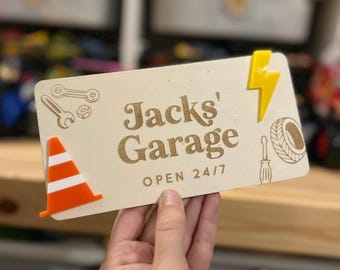 May include: A wooden sign with the text "Jacks' Garage" and the words "OPEN 24/7". The sign has a yellow lightning bolt, an orange traffic cone, and other garage-themed graphics.