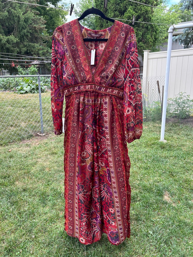May include: A long, red, and purple patterned maxi dress with long sleeves and a V-neckline. The dress has a fitted bodice and a flowing skirt. The fabric is sheer and lightweight.
